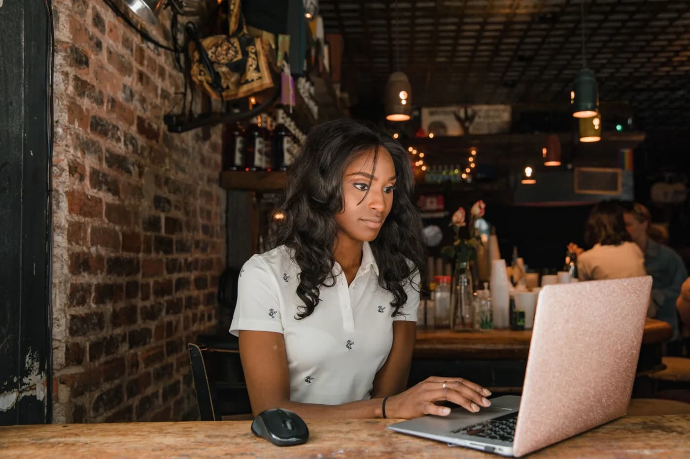 A woman working on her laptop at a wooden table in a warm, brick-walled café