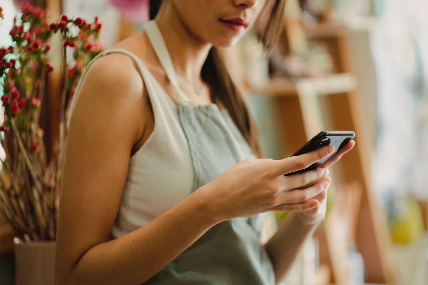 A florist in an apron using a smartphone beside flowers in her shop