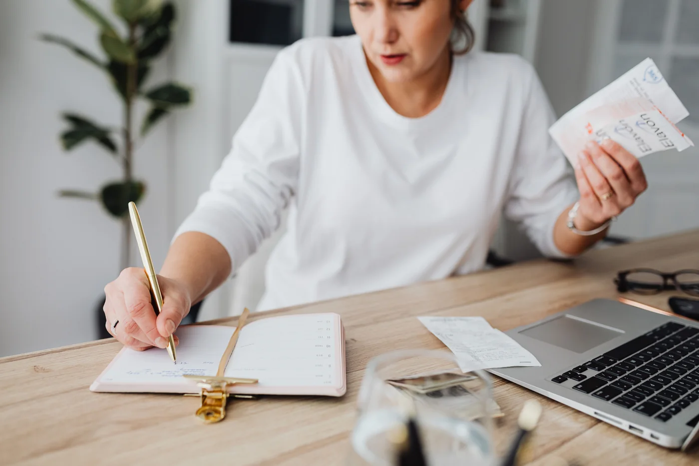 A woman checking receipts and writing in a notebook beside her laptop