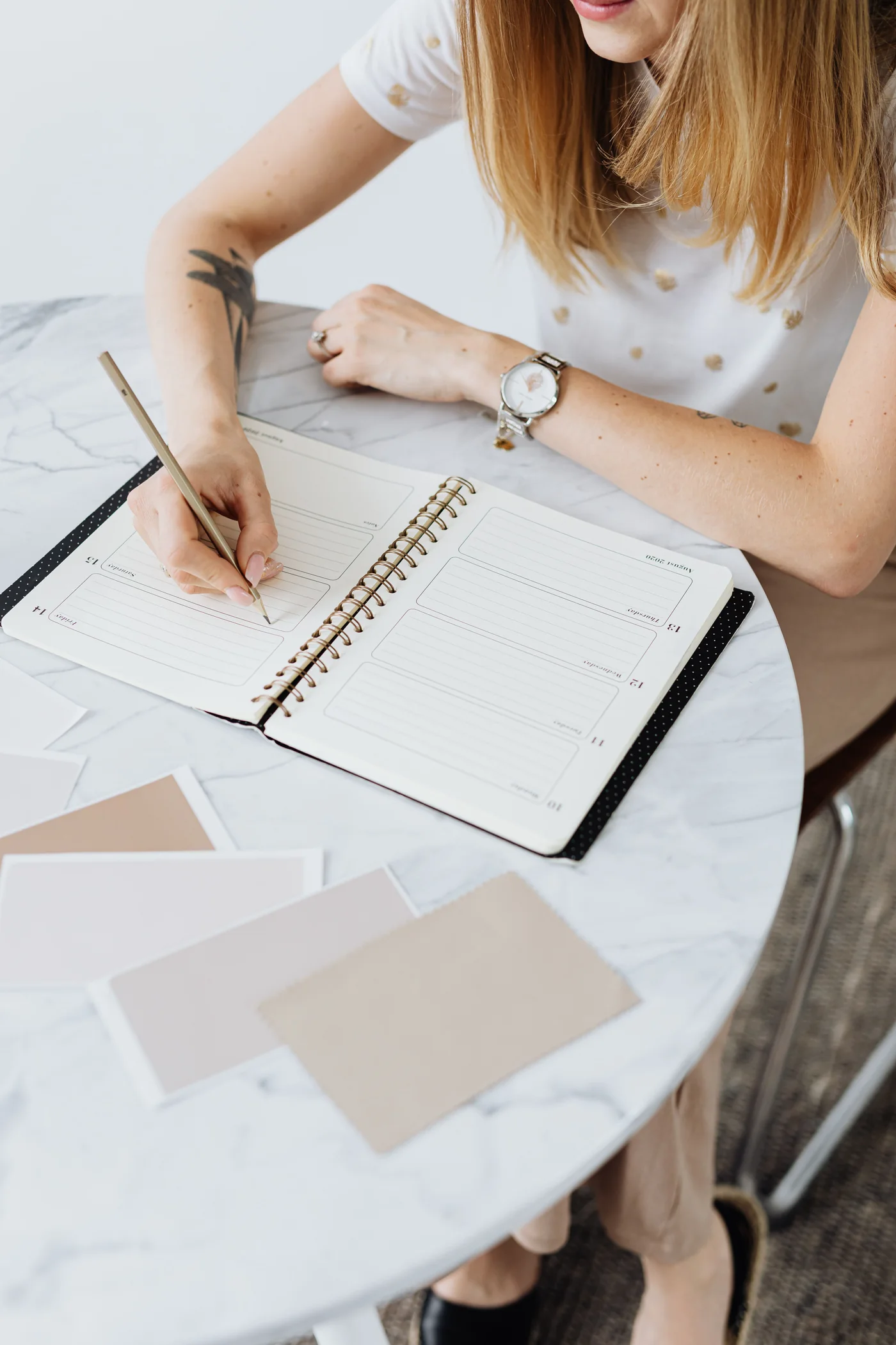 A woman writing in a weekly planner beside neutral colour samples
