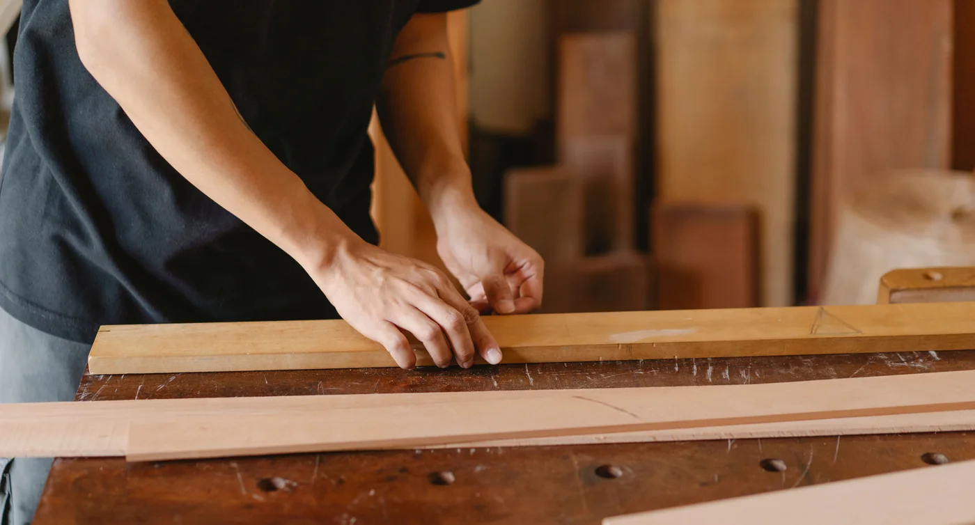 A carpenter measuring a wooden plank on a workshop bench